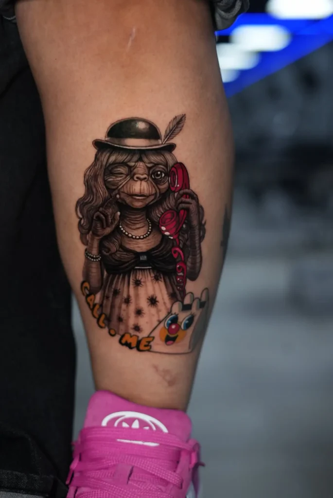 E.T. con bombín, collar de perlas y teléfono rojo tatuado a color en la pierna