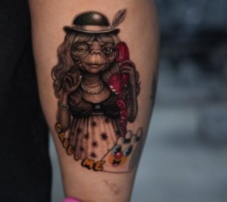 Tatuaje a color de E.T. con bombín · Samantha E.T. con bombín, collar de perlas y teléfono rojo tatuado a color en la pierna