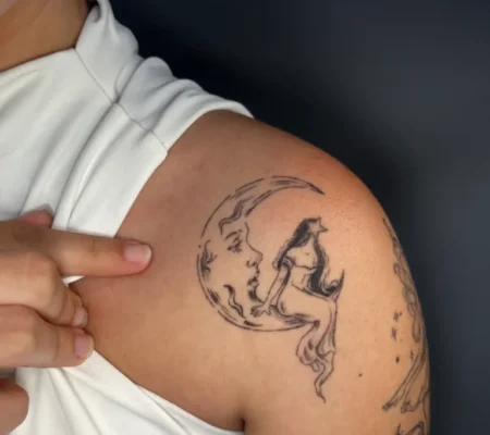 Tatuaje fine line de luna con figura sentada · Dennys Luna con una figura sentada, en fine line, en el hombro