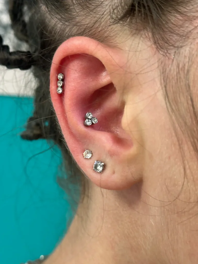 Oreja con piercings de brillante en el hélix, el conch y el lóbulo